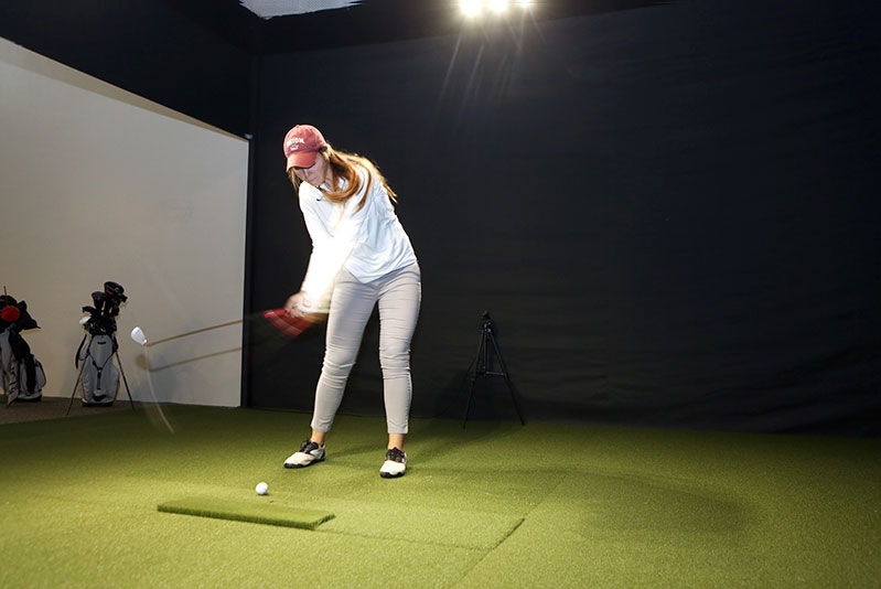 A student perfecting her golf swing at an indoor golf practice simulation.