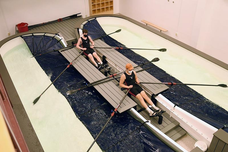  Male crew members honing their skills in a rowing tank at the Alumni Gymnasium.
