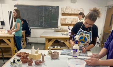Students working in clay with some of their creations displayed on a table.