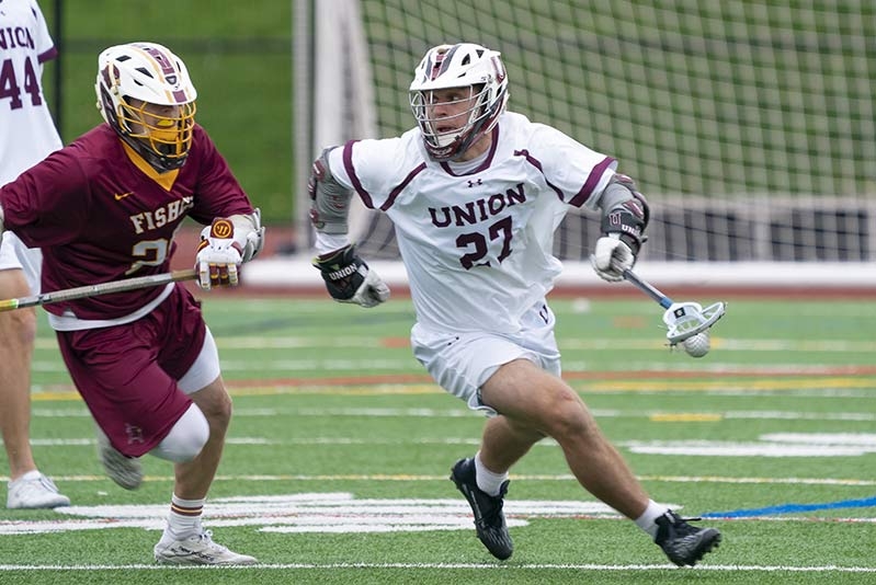A Union lacrosse player on the men's team, holding the ball, tries to evade an opponent.