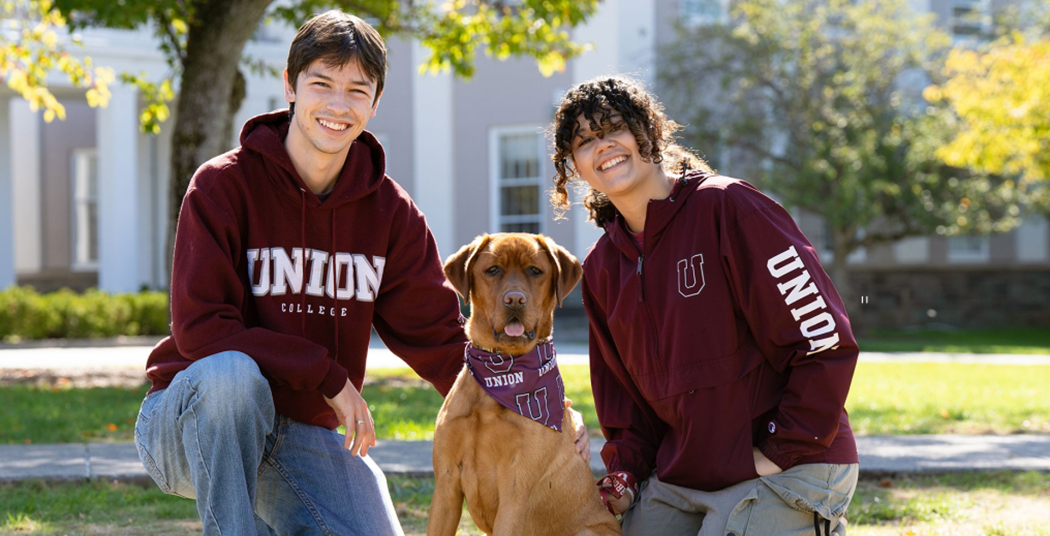 two students sitting with a red fox lab named Charger