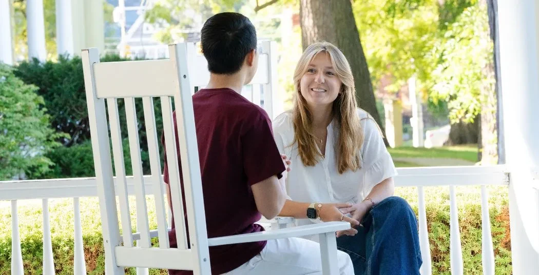 A Union student interviewing a candidate for admission. They're sitting in Adirondack chairs facing each other, on the front porch of Admissions. 