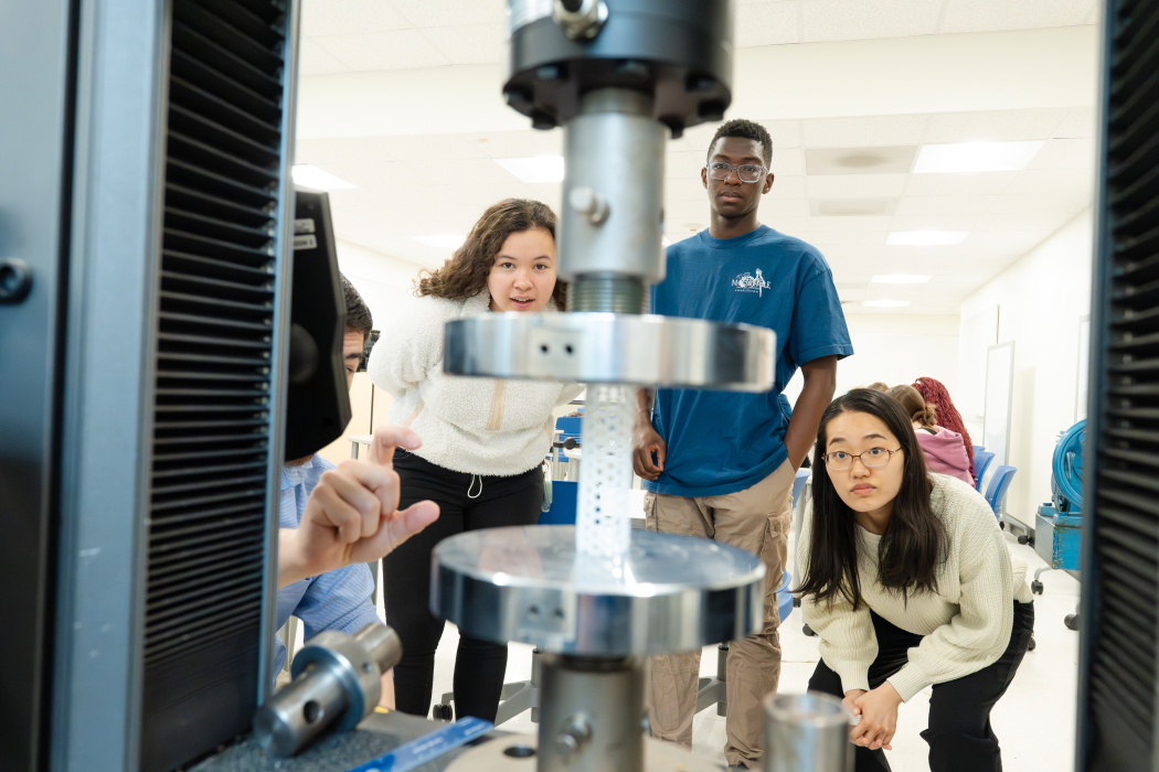 Biomedical engineering students observing a 3D printed stent in a mechanical testing machine. 