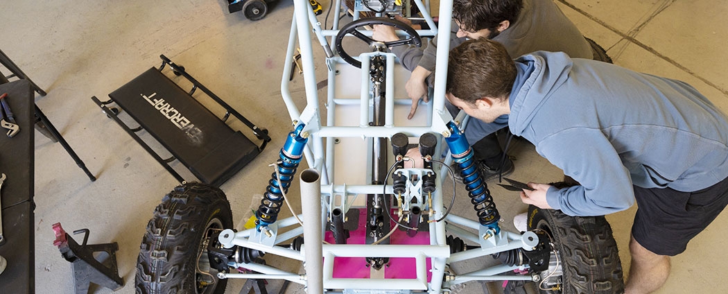 Students are working on one of the Baja off-road vehicles in a garage