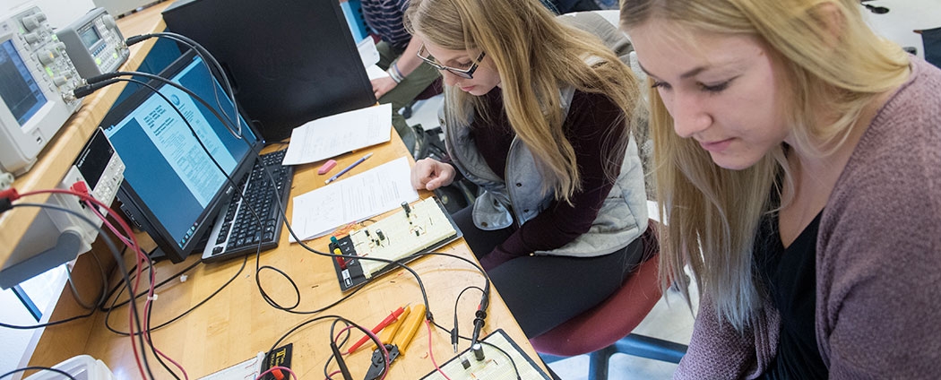 Two students in an electrical engineering classroom are working with testing equipment.