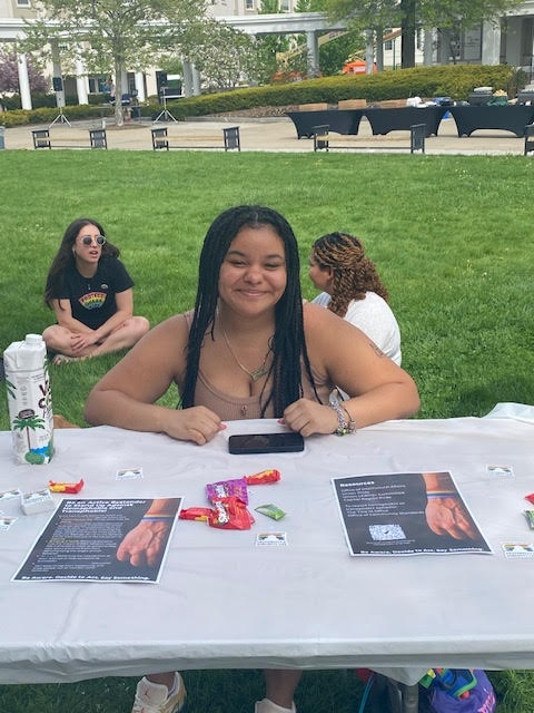 Ginde Baker, English and Spanish Double Major, Class of 2023, seated at a Pride Fest table.