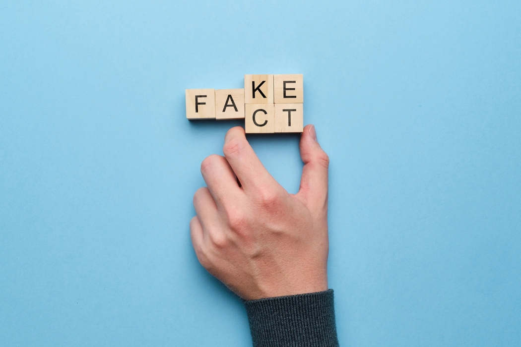 Hand moving 2 scrabble cubes to change the word "fact" to "fake"