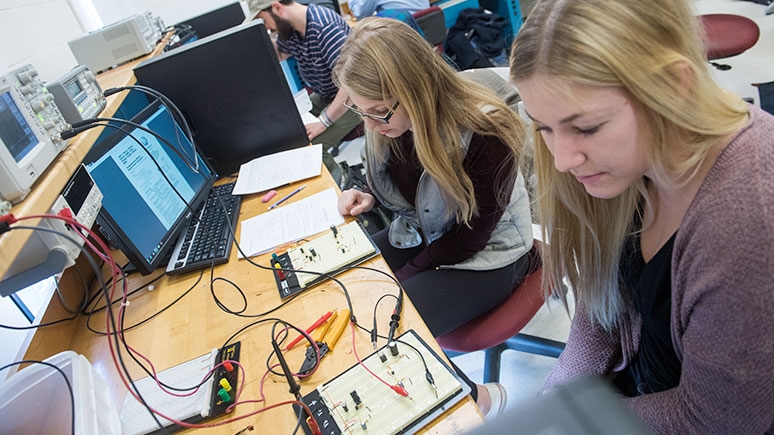  Two students examining electronic equipment as a component of their engineering course.