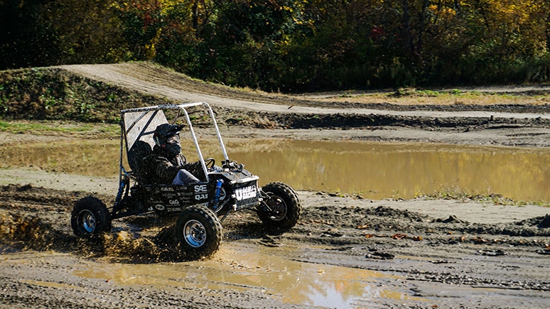A sleek car, crafted by engineering majors at Union College, speeds through the muddy terrain
