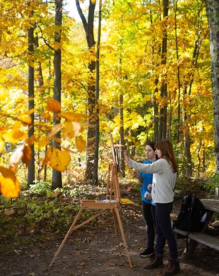 A student painting in Jackson's Garden as a professor looks on