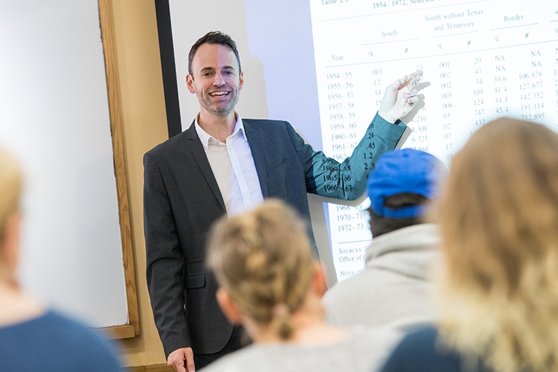 Political Science professor Bradly Hayes gestures toward a screen while teaching a class.