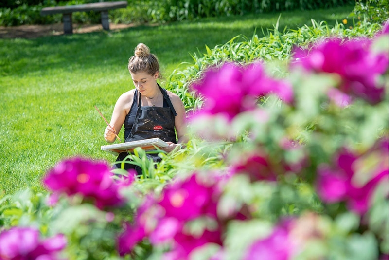 A student painting a canvas will seated on the ground in Jackson's Garden.