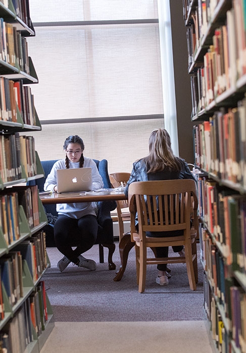 Two students studying near library book stacks