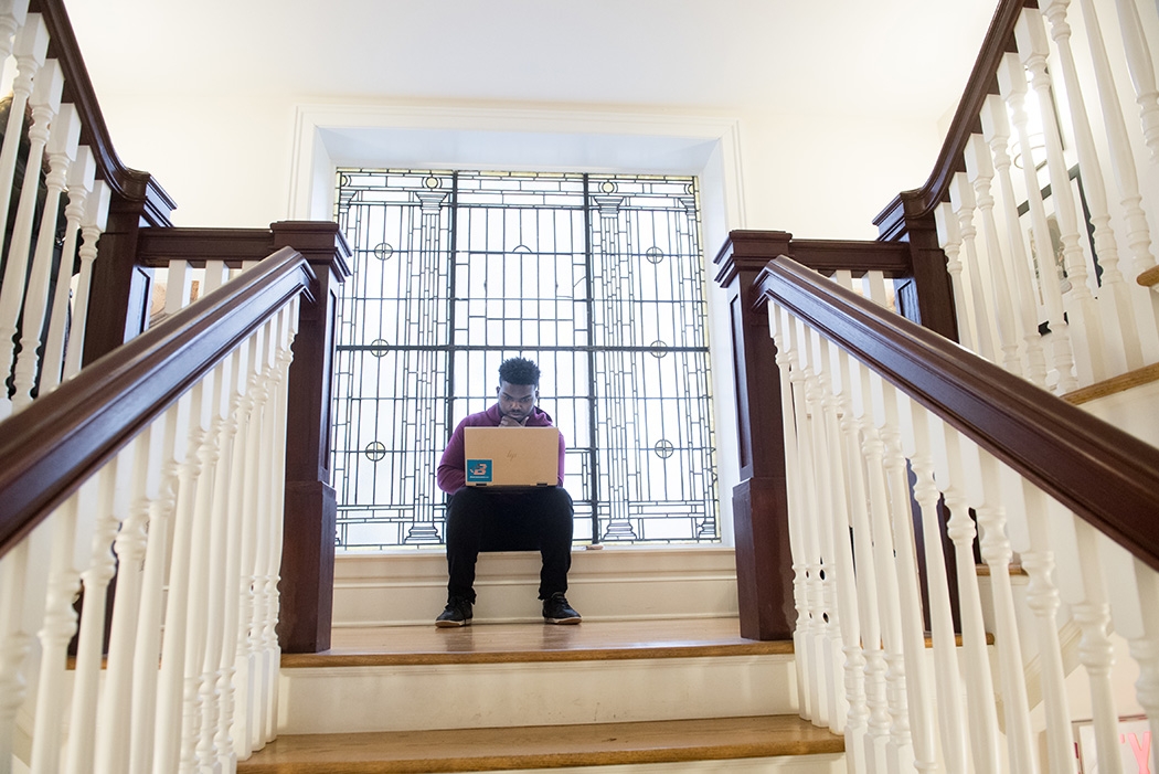 Student Luis Mota viewing his laptop while sitting at one of the landings of a Lamont House staircase.