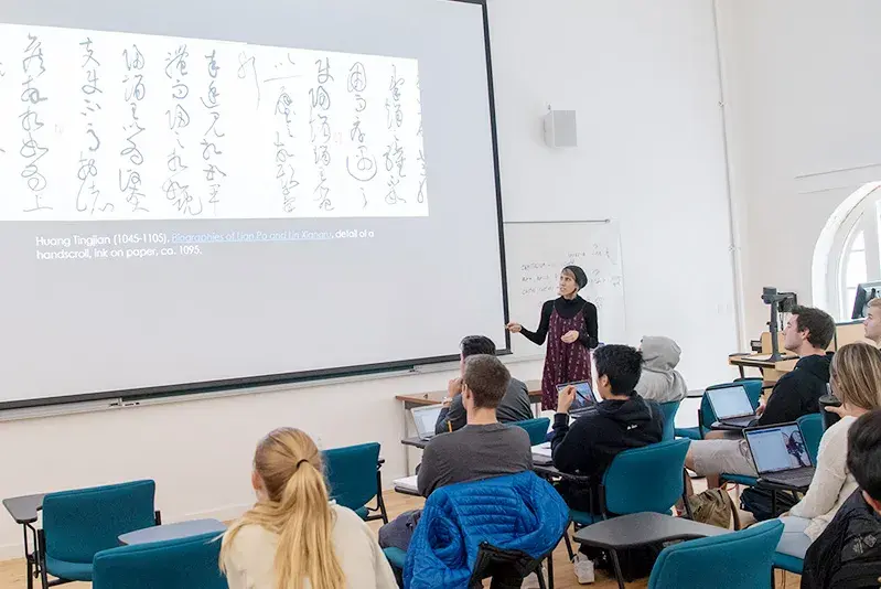 Art Professor Sheri Lullo gestures to a screen on which is projected Chinese calligraphy.