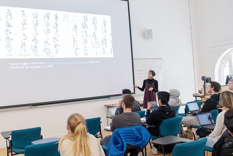 Art Professor Sheri Lullo gestures to a screen on which is projected Chinese calligraphy.