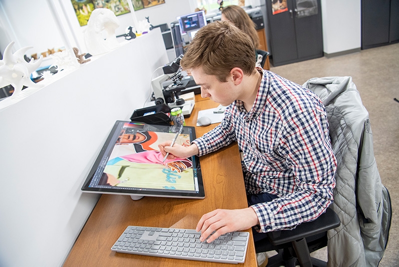 A student in the digital classroom creating art on a computer pad.