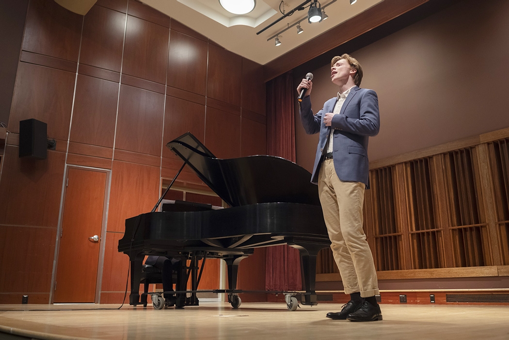 A student singing on stage in the Emerson Auditorium