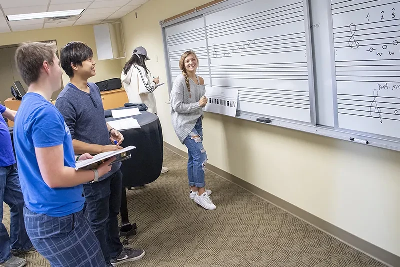 As pat of a music classroom exercise, a student writes music composition notes on a whiteboard.