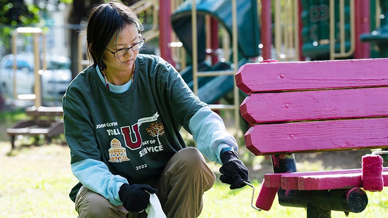 A student volunteer painting a playground bench.