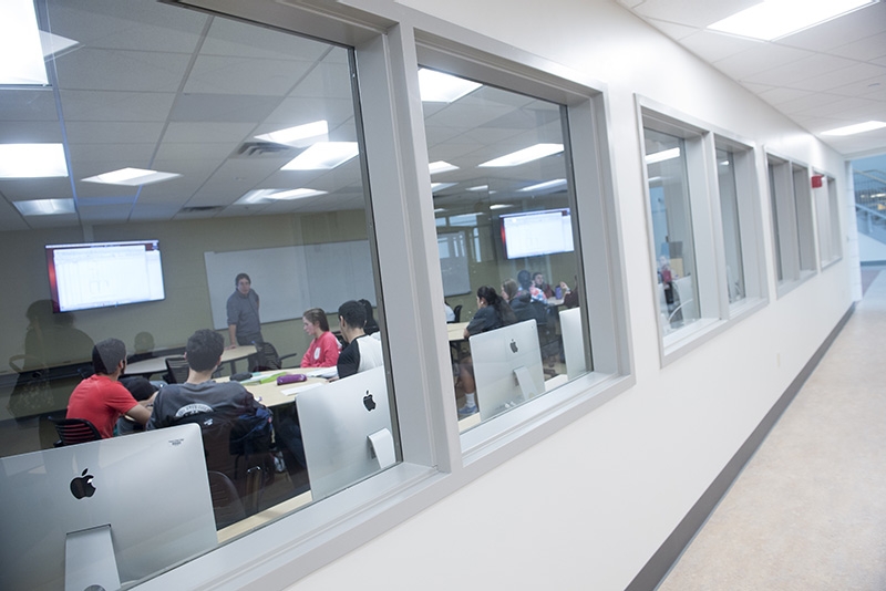  A perspective of a classroom seen through glass windows from a hallway.