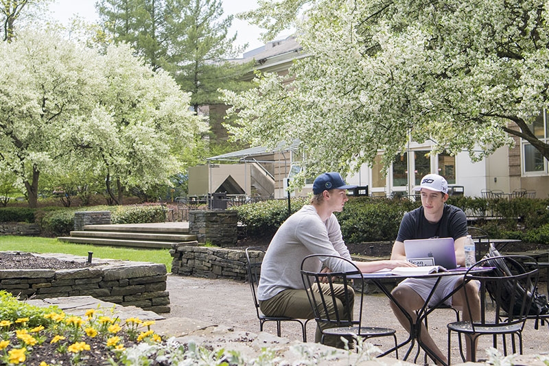 Students seated outside in the back of Reamer Campus Center.  Trees in bloom are visible in the background.