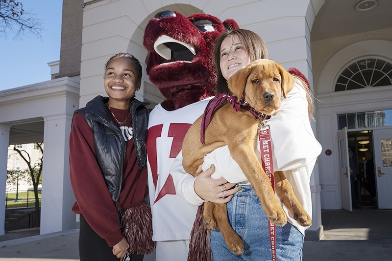 Students pose with the costumed mascot as one of them holds a puppy.