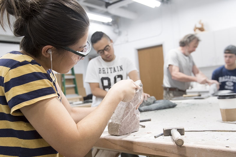 A student sculpting a piece of stone in an art class.