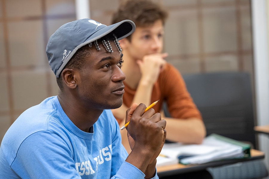 A student sitting at a desk and holding a pencil listens intently