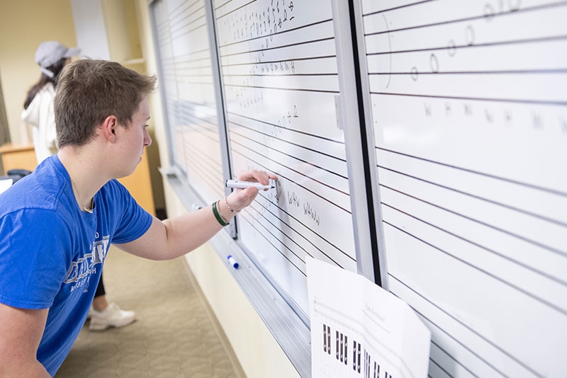 A student write some musical notation on a white board.