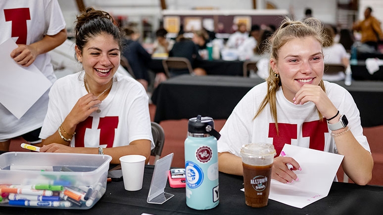 Two students staffing a table in the Field House.  The students are participants in a community service event. 