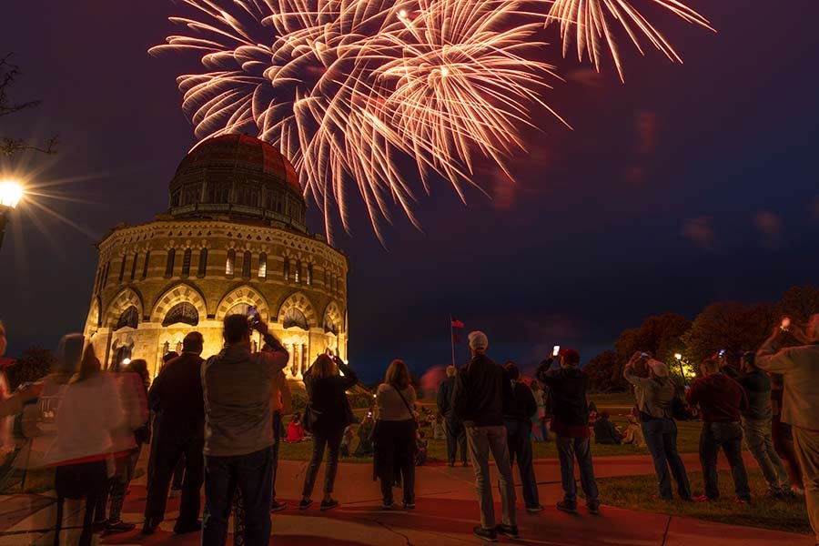 A crowd looks at fireworks exploding above the Nott Memorial.