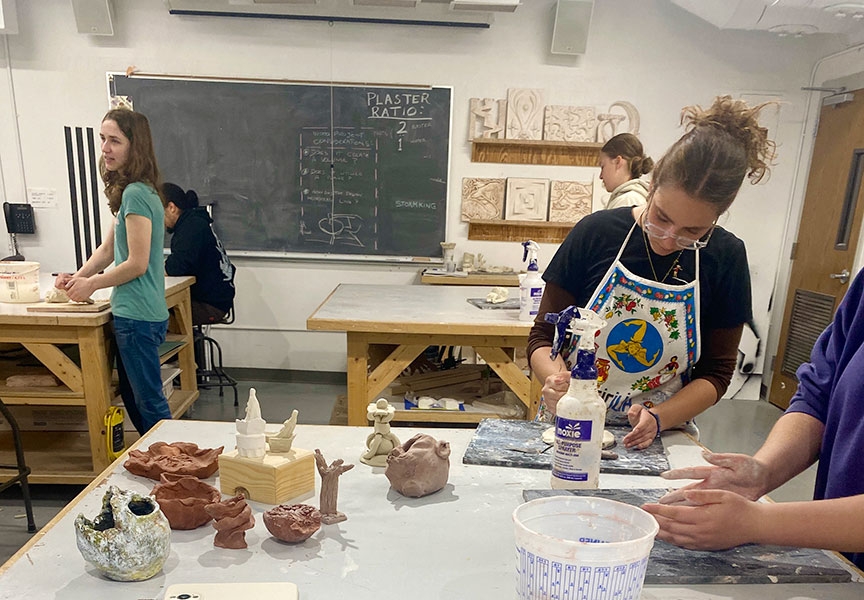 Students working in clay with some of their creations displayed on a table.