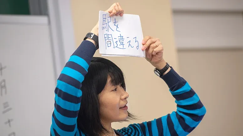 A Japanese teacher holds up a card with Japanese writing