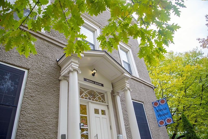 A view of the front door of Messa House with tress in all their autumnal glory visible to the side.