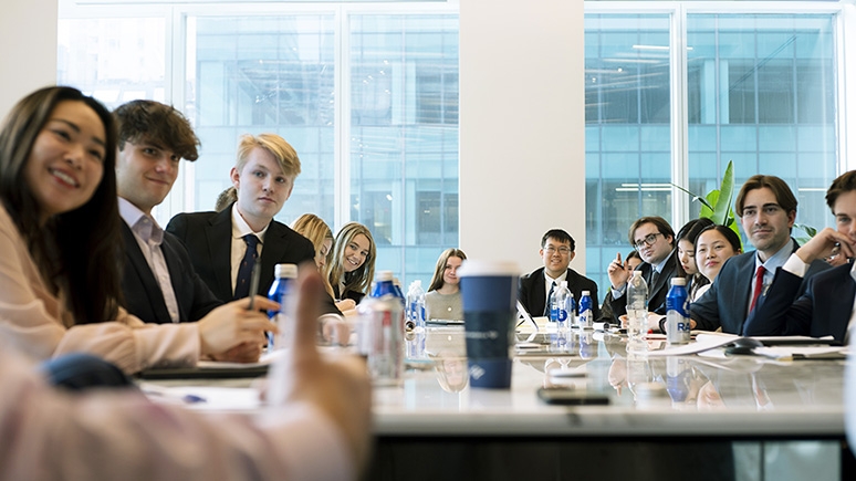Students gathered around a table listen attentively to an off-camera speaker during a finance bootcamp in New York City