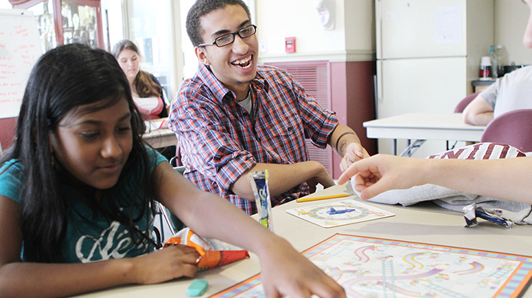 A student smiles as he looks on as a young girl moves pieces on a game at the Kenney Community Center