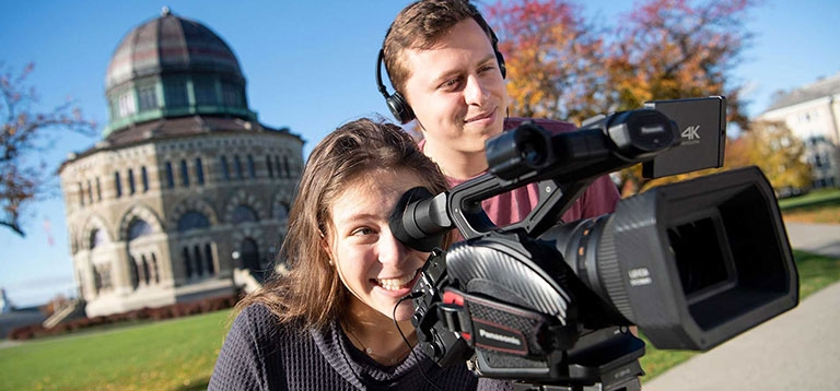 Two students peering through a video camera