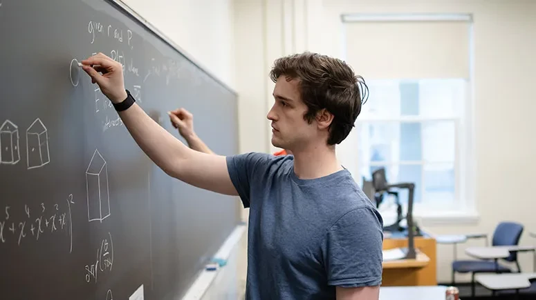 A student writing a math equation on a blackboard