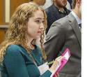 Student with a clipboard and notepaper listens attentively to a representative of a local employer.