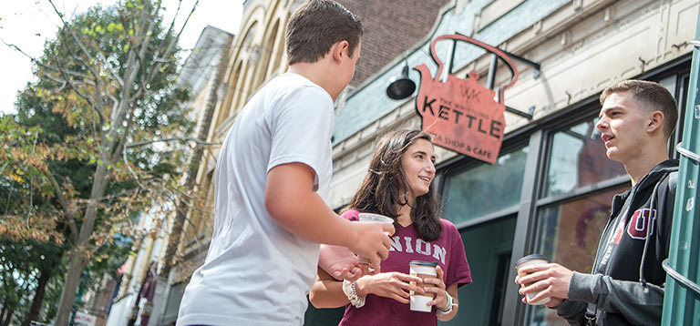 Students standing outside the Whistling Kettle Restaurant drinking coffee