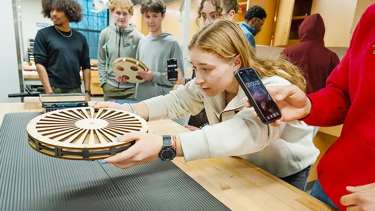 A student carefully places a disk above a platform during a magnetic levitation experiment.