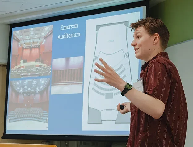 Alex Roginski ’26 stands in front of a screen while explaining his research on architectural acoustics.