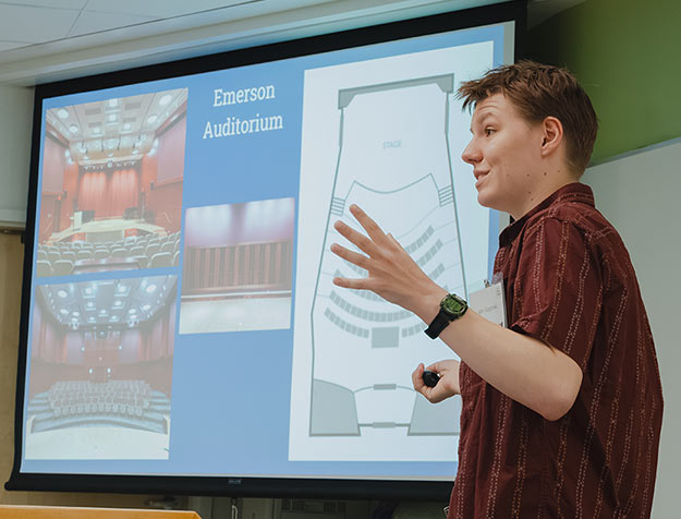 Alex Roginski ’26 stands in front of a screen while explaining his research on architectural acoustics.