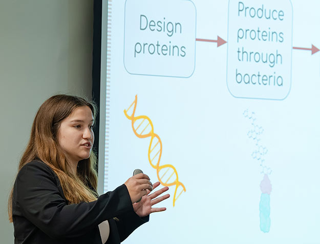 Elizabeth Bias ’26 stands in front of a projection while explaining her research in a laboratory working to develop a vaccine for Lyme disease.