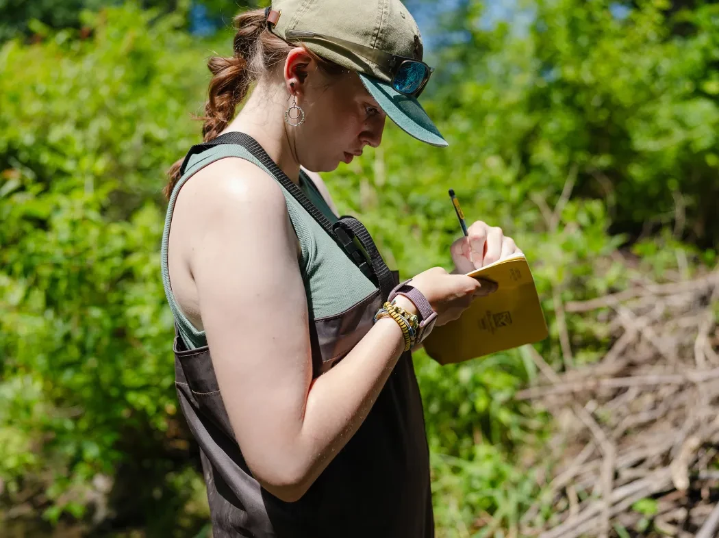 a woman writes in a journal outside in the bright sun