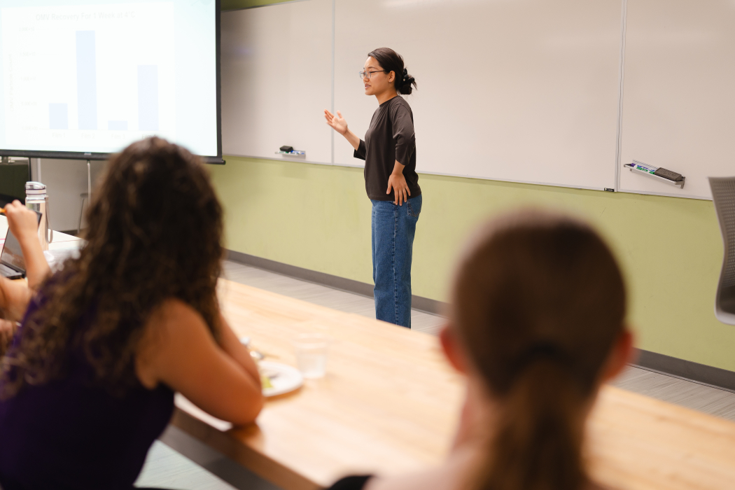 A woman stands at the front of a classroom talking.