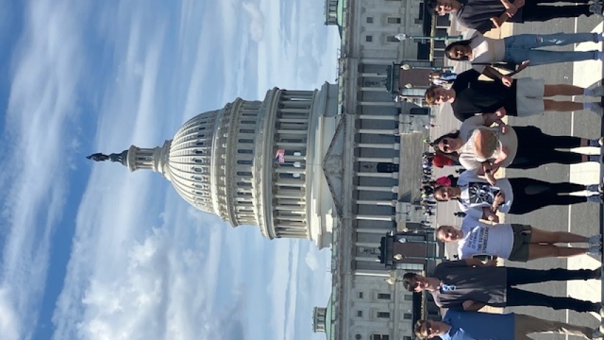 A group of 8 students linking arms while standing in front of the Capitol Building in Washington D.C.
