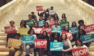 Students and staff with signs sitting on the stairs at the State Capitol in Albany