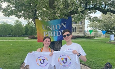 Two Union students standing in front of a rainbow colored Union Pride flag.